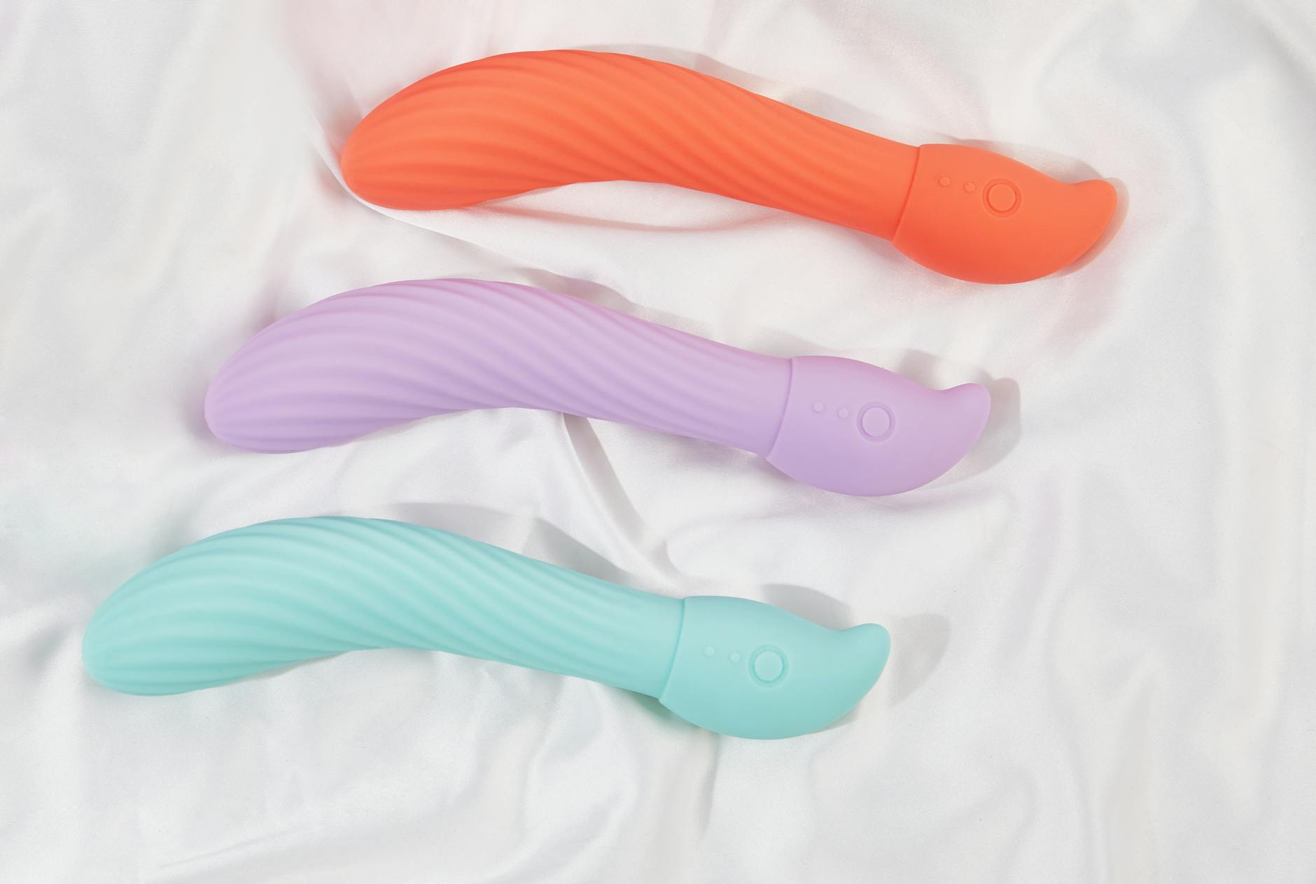 Three colorful clitoral vibrators arranged on soft fabric, highlighting their smooth rounded design