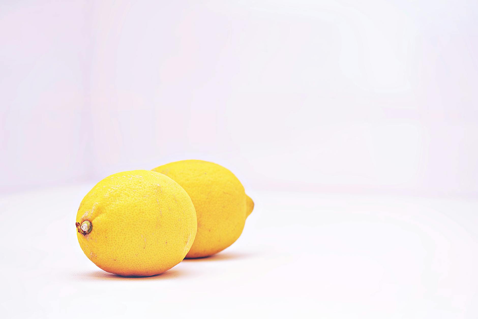 Two vibrant lemons on a minimalist white background, symbolizing freshness and natural pleasure
