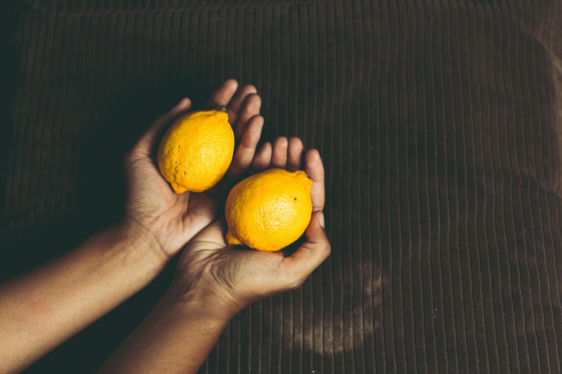 Close-up of two fresh lemons held in cupped hands, symbolizing the gentle suction design of lemon clitoral vibrators