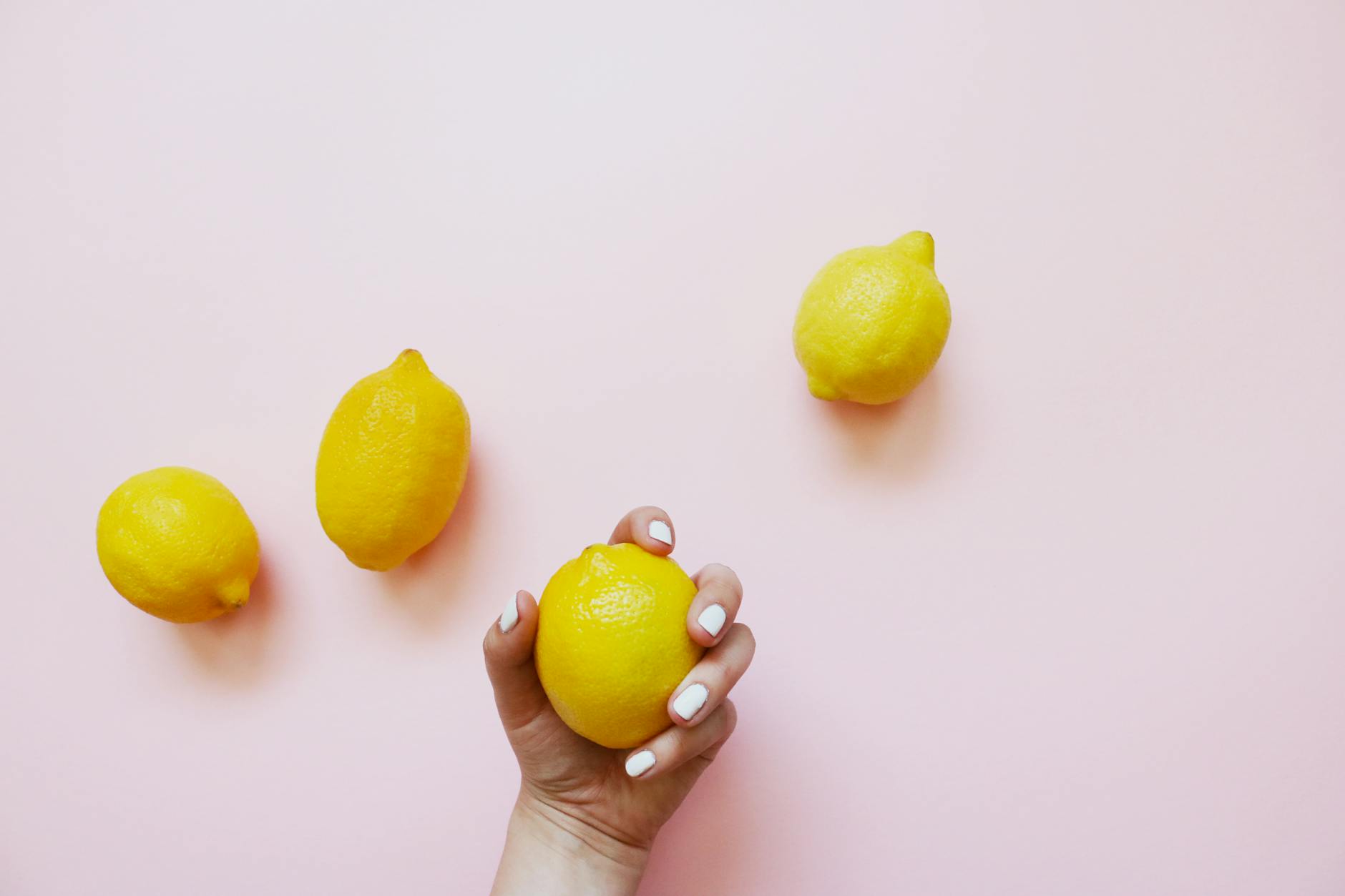Hand holding a lemon on soft pink background, symbolizing gentle reconnection and renewal