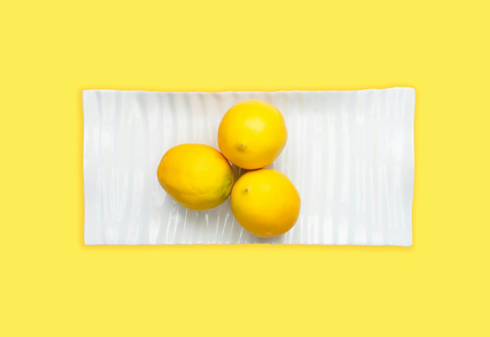 Fresh lemons arranged on a white plate with vibrant yellow background, symbolizing renewal and vitality