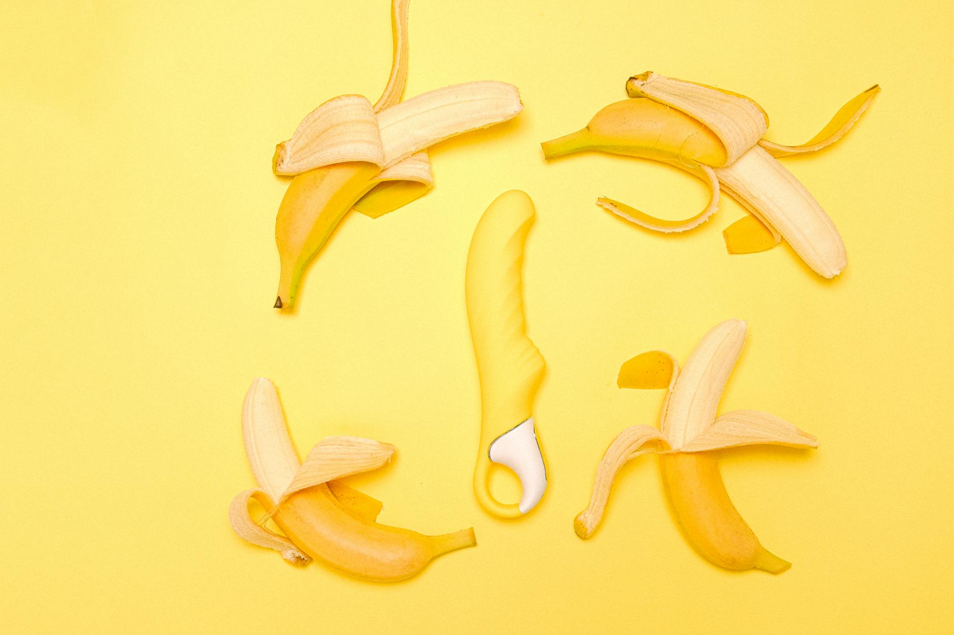 Yellow silicone vibrator surrounded by fresh lemons on bright yellow background