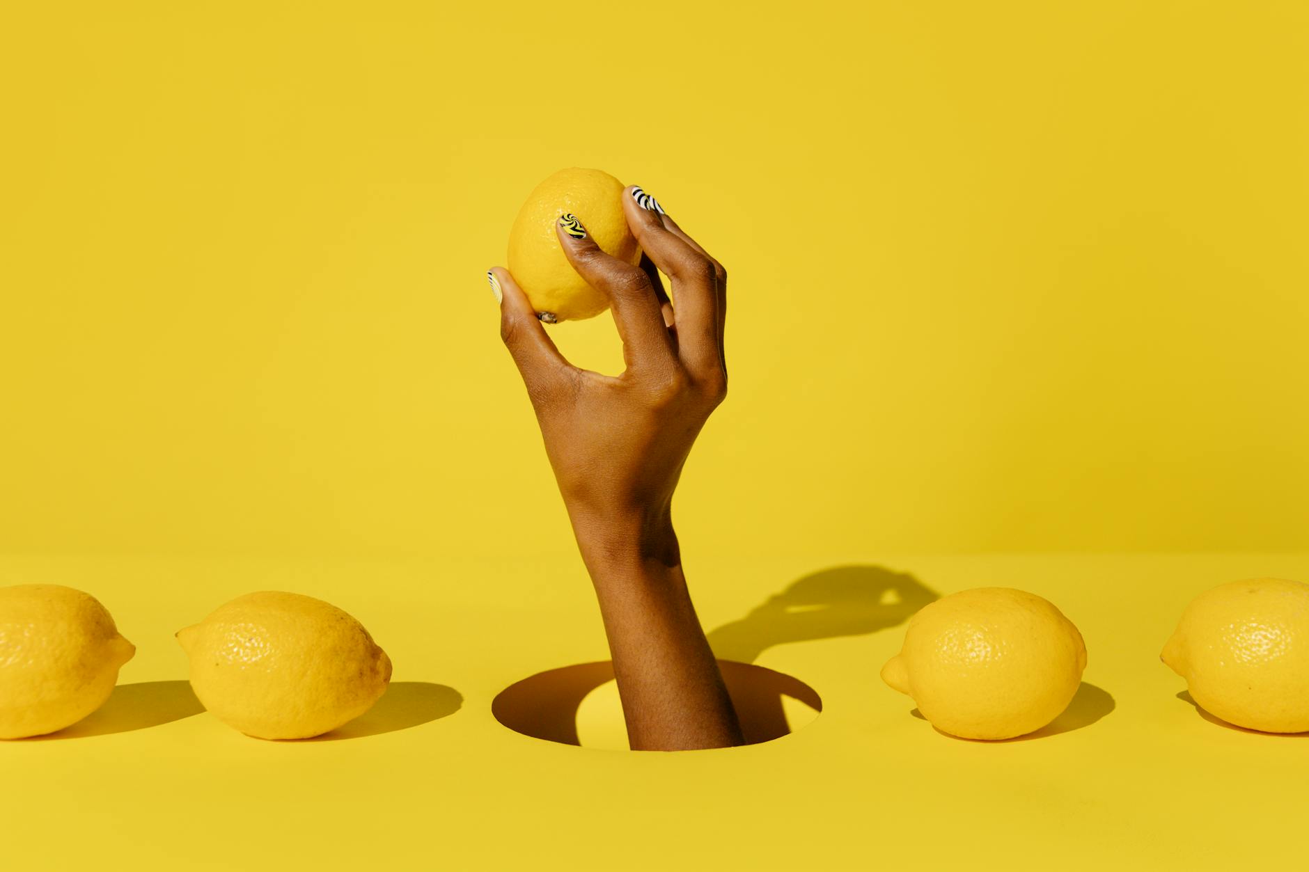 A hand holding a fresh lemon against a bright yellow background, symbolizing the vibrant energy of pleasure and vitality