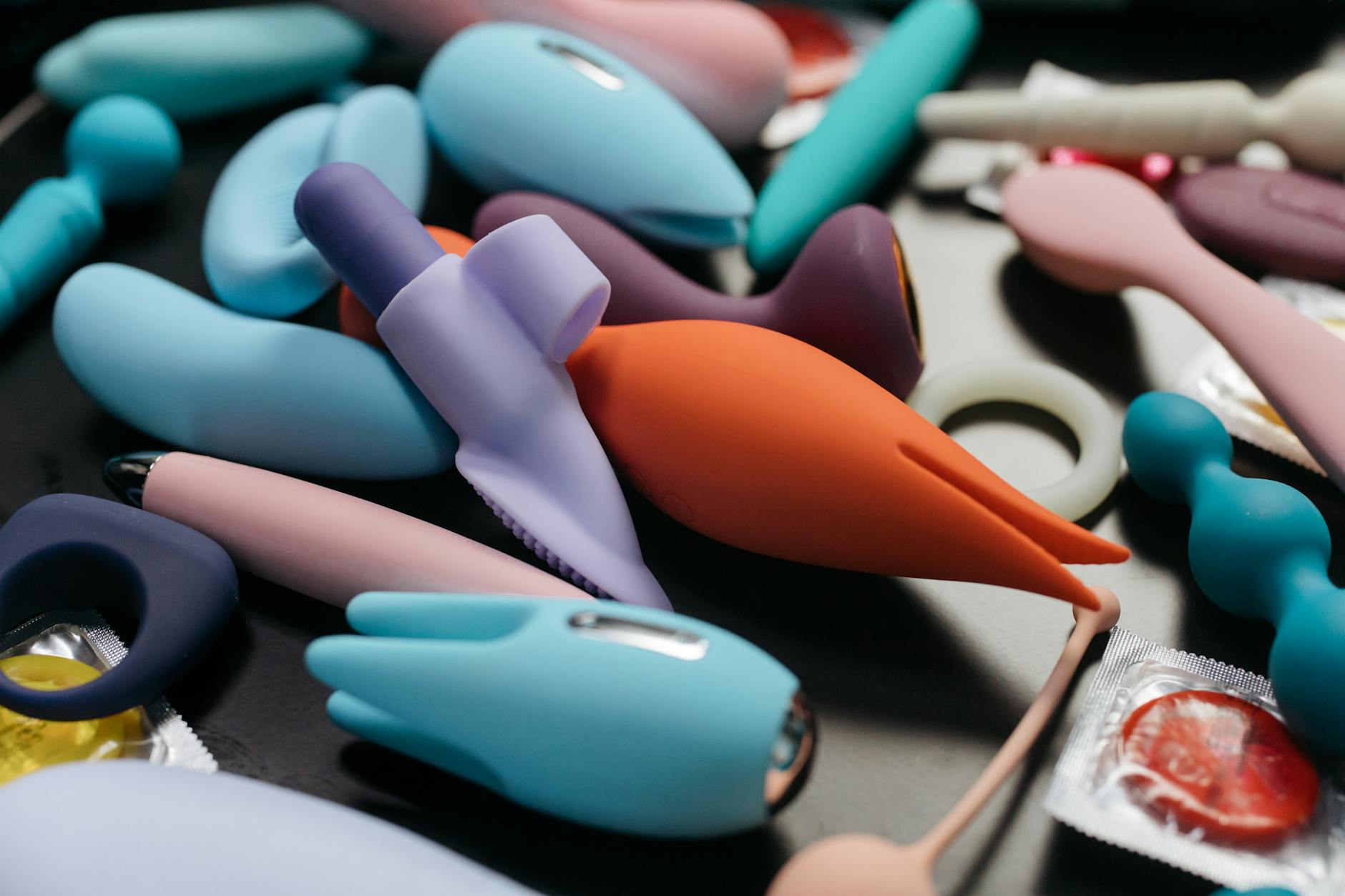 Two hands holding pink and blue clitoral vibrators against a soft pastel background