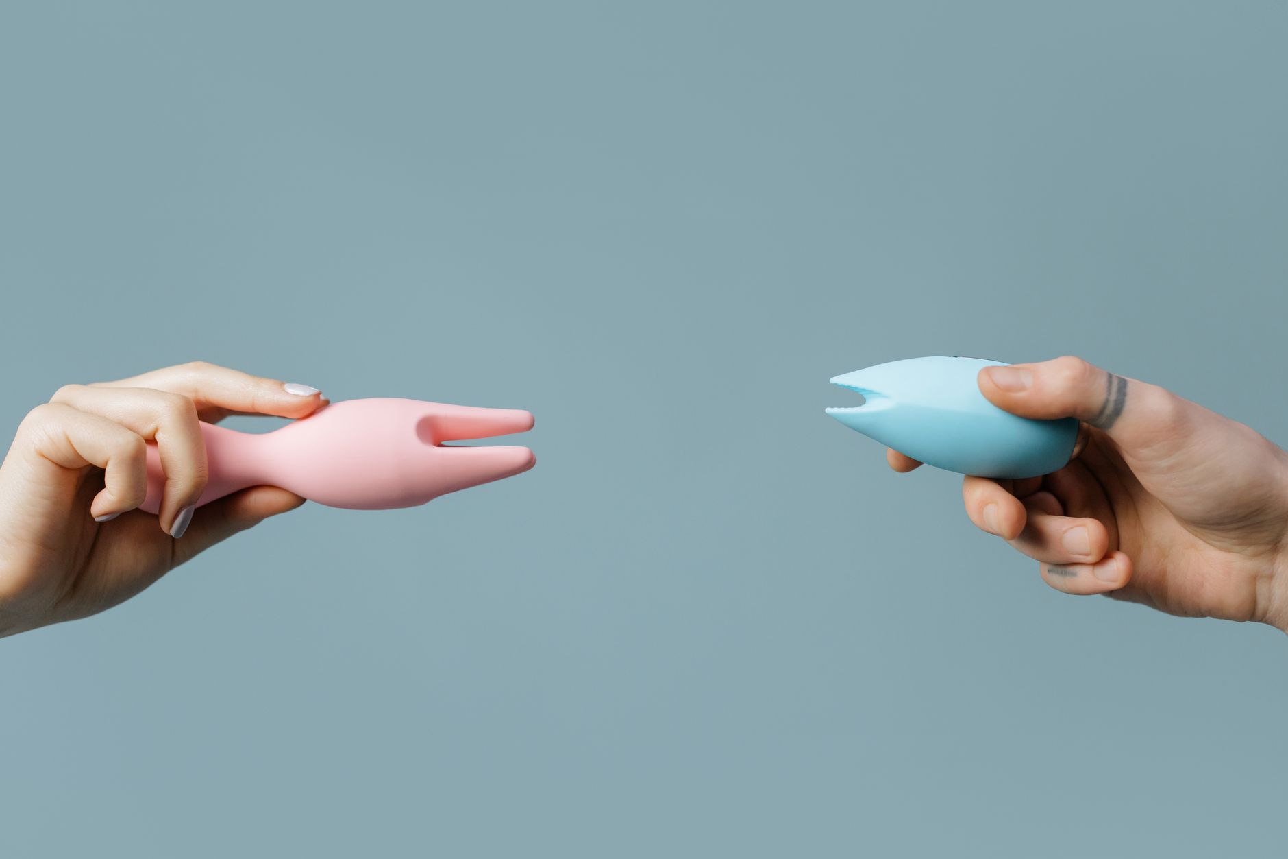 Hands holding pink and blue silicone lemon vibrators on a soft pastel background