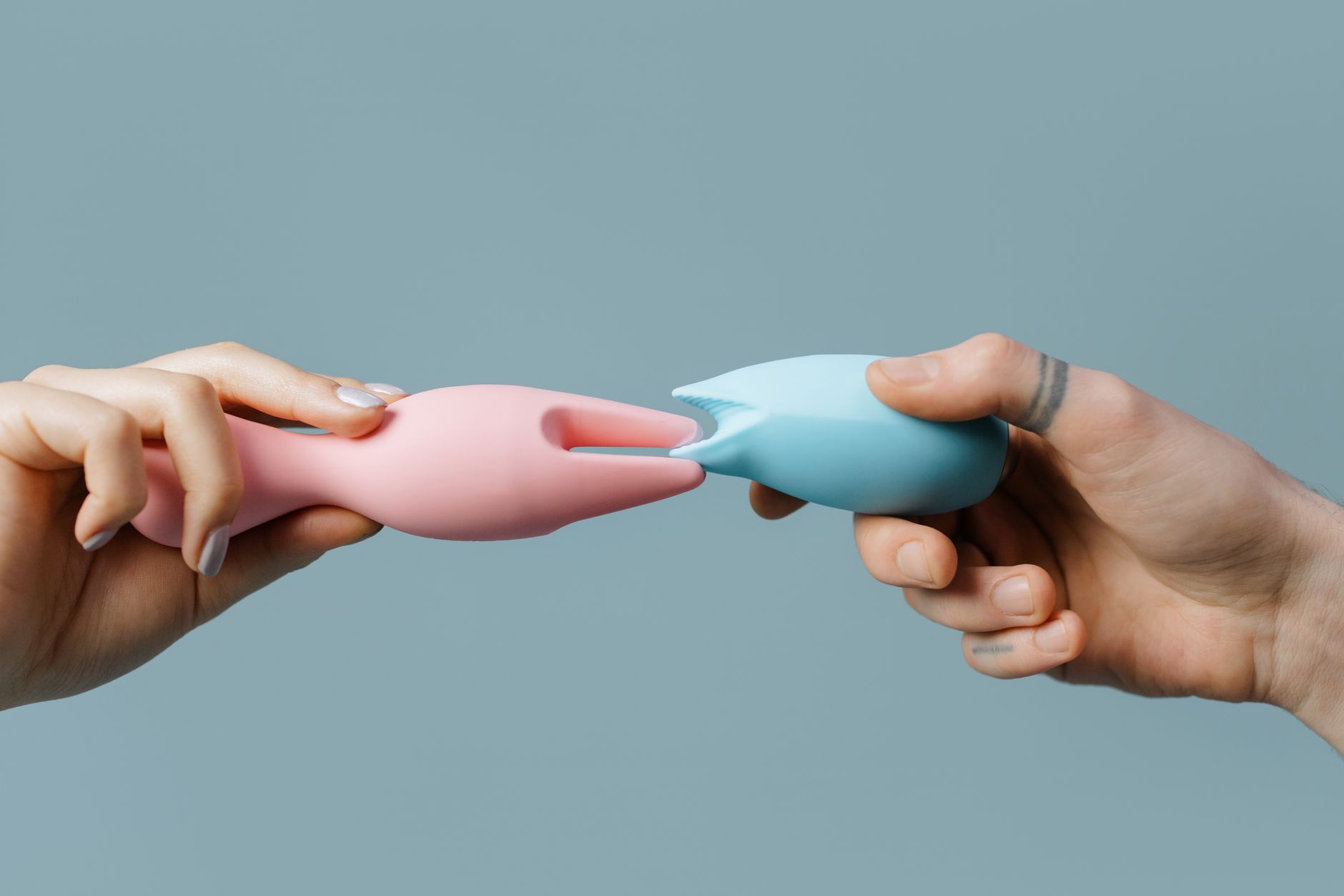 Hands holding colorful silicone vibrators against a neutral background, symbolizing reclaimed pleasure