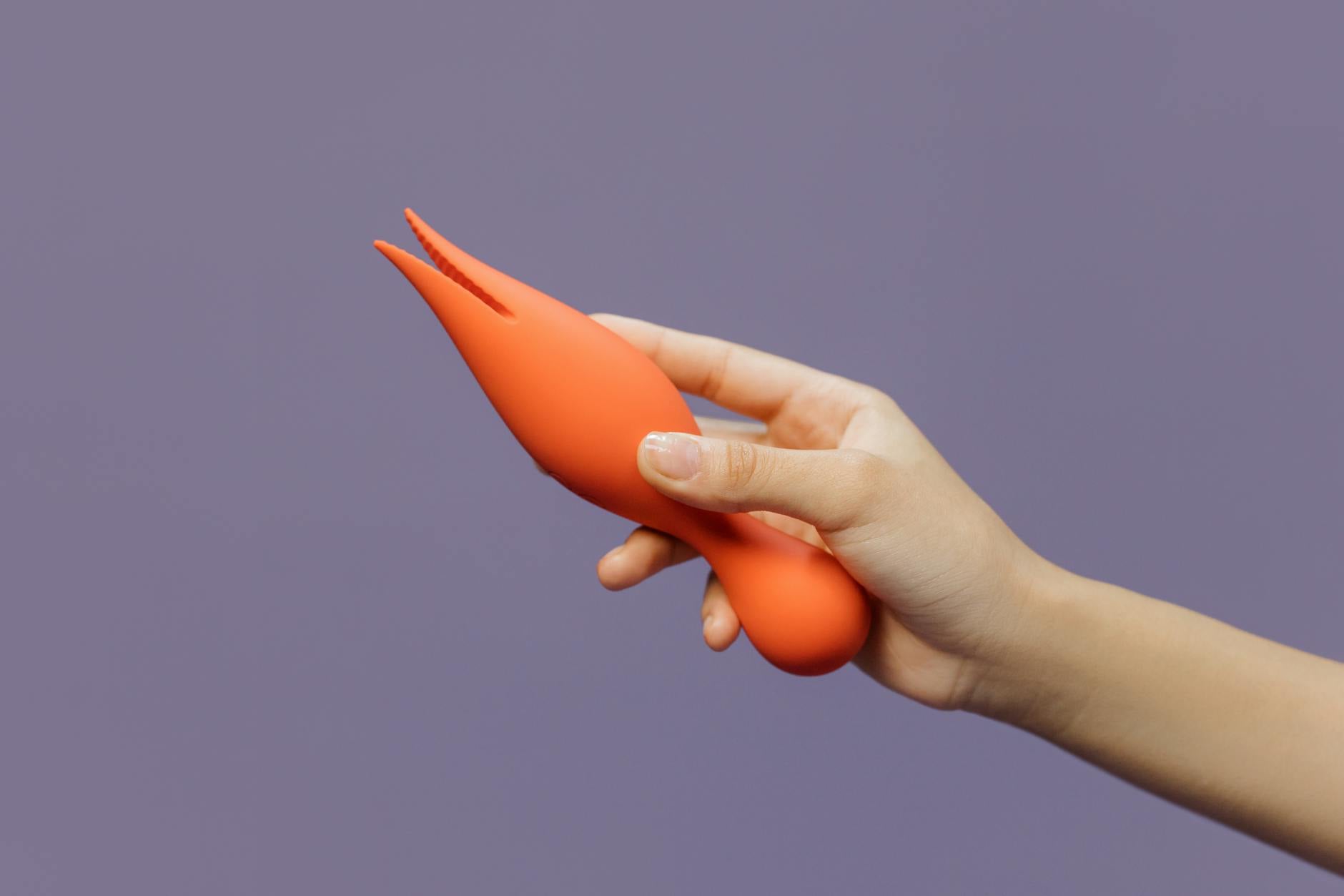 A close-up of a hand holding a colorful vibrator against a minimalistic purple backdrop, showcasing modern sensuality and pleasure.