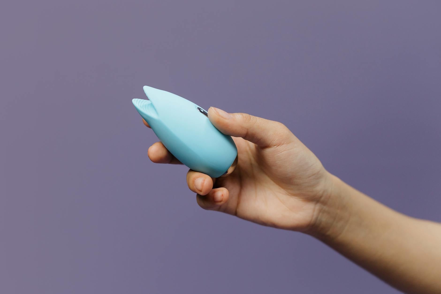 A person holding a blue silicone vibrator against their hand, representing pleasure and self-discovery