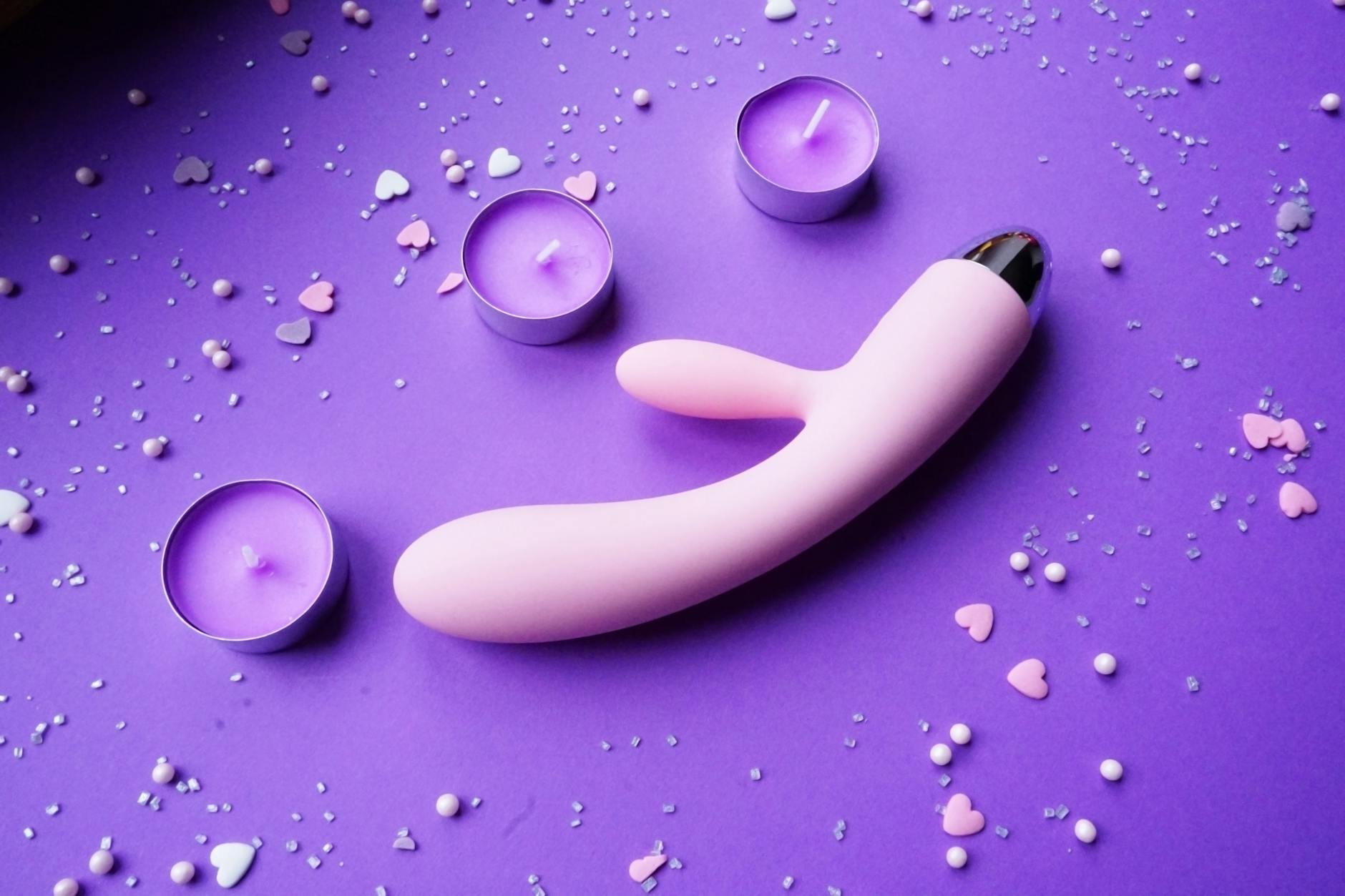 Pink lemon vibrator on purple background with heart confetti and candles for a romantic, intimate mood